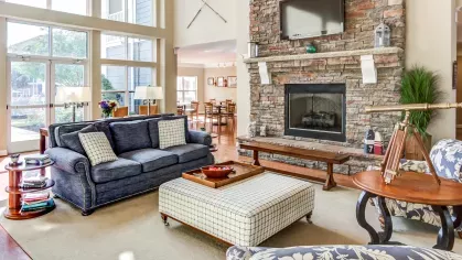 Spacious clubhouse lounge with large windows, stone fireplace, and blue upholstered seating