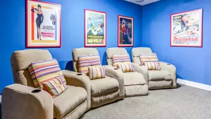 Theater room with four beige recliners and colorful striped pillows, set against a bright blue wall with classic movie posters