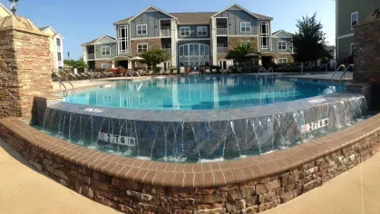 Infinity-edge pool with cascading water feature and stone pillars, in front of a luxury apartment building