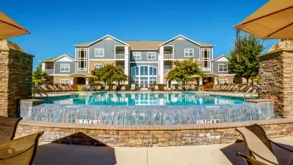 Clubhouse and pool view framed by stone columns and patio chairs under large umbrellas