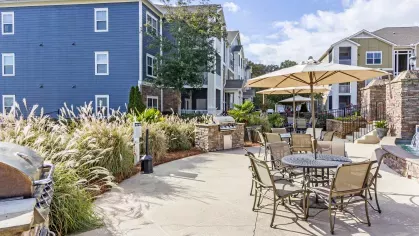 Grill and patio area with umbrella-shaded tables and lush landscaping