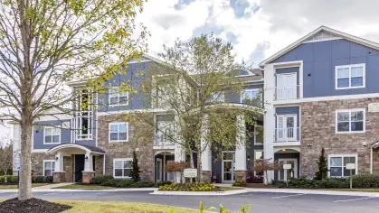 Leasing office entrance framed by mature trees, flowers, and apartment community signage