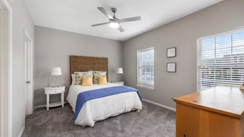 Primary bedroom with woven headboard, plush carpet, and large windows at Lauren Ridge.