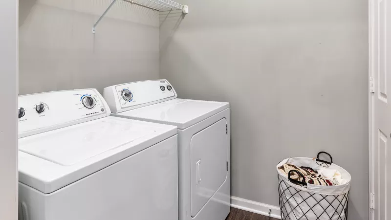 Laundry room with full-size washer and dryer and ample shelving at Lauren Ridge.