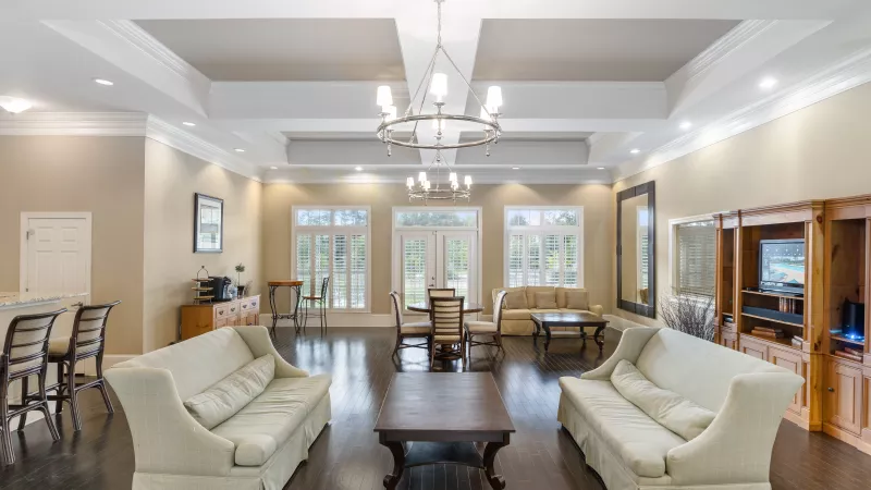 Spacious resident lounge at Lauren Ridge Apartment Homes featuring plush seating, large windows with white shutters, elegant chandeliers, and hardwood flooring.
