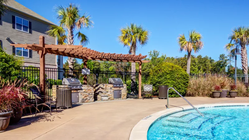 Resort-style outdoor grilling station at Lauren Ridge featuring stone countertops, dual stainless steel grills, and shaded pergolas surrounded by palm trees.