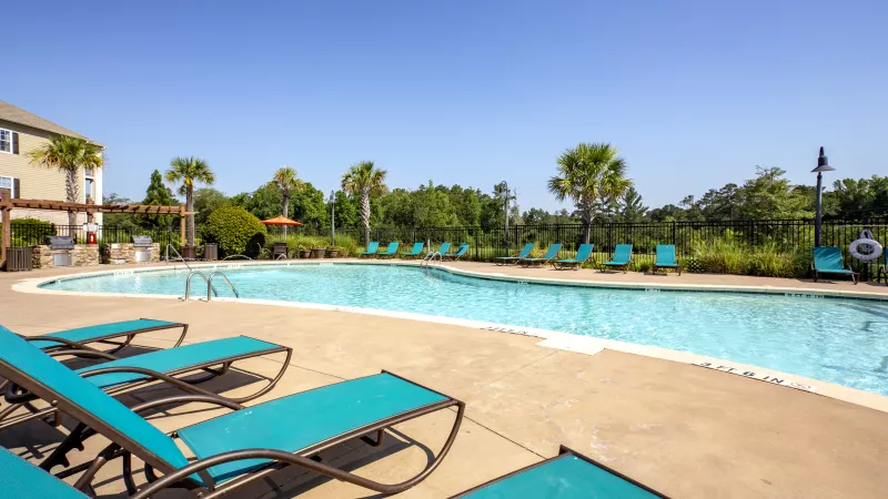 Serene swimming pool area with tropical landscaping and ample lounge seating at Lauren Ridge Apartments, perfect for relaxing in the sun.