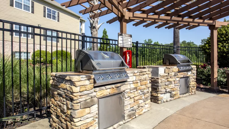 Close-up of outdoor grilling station with stone base and stainless steel appliances beneath a wooden pergola at Lauren Ridge community area.