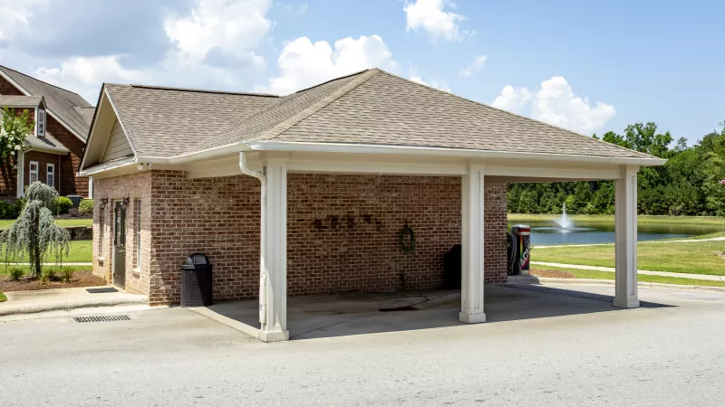 Covered brick car wash station with hose and vending machine at Lauren Ridge Apartment Homes, near a scenic pond with fountain.