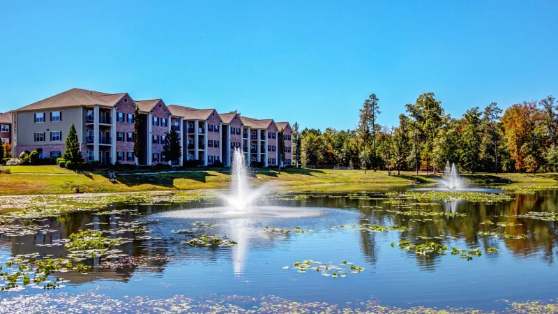View of Lauren Ridge Apartment Homes’ brick and siding exterior with balconies, overlooking a large pond with central fountain.