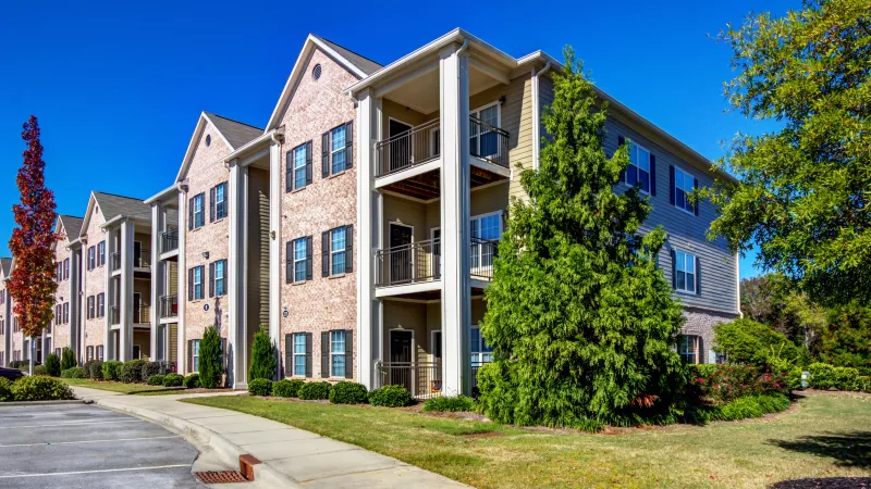 Sidewalk and landscaped front of Lauren Ridge’s three-story apartment building with red brick and beige siding facade.