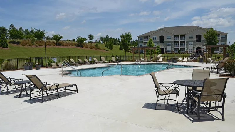 Poolside seating area with lounge chairs and tables, overlooking the swimming pool and landscaped grounds.