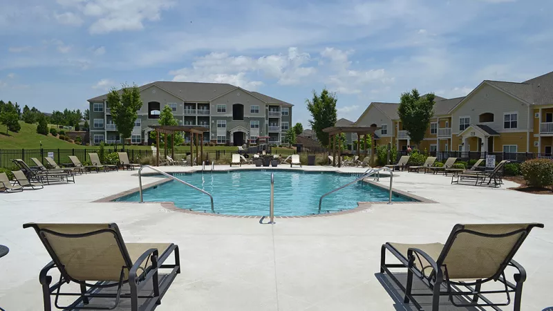 Wide view of the sparkling pool framed by apartment buildings and shady pergolas.