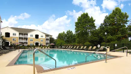 Large outdoor pool at Reed Creek Apartments with poolside loungers and landscaped greenery for resident relaxation.