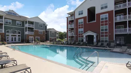 Sparkling pool adjacent to red and green apartment buildings at Reed Creek Apartments, ideal for cooling off on sunny days.
