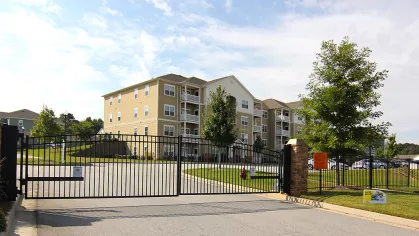 Gated entrance to Reed Creek Apartments with keypad access and multi-story beige and white apartment buildings in the background.