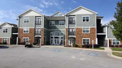 Main leasing office building at Reed Creek Apartments featuring stone and siding exterior with arched glass entrance and accessible parking spaces.