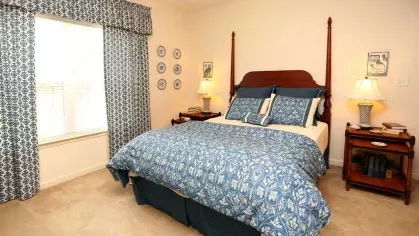 Sunlit bedroom with large window, matching blue curtains and comforter, and traditional wooden bed frame