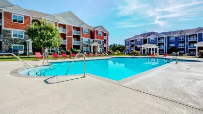 Sparkling community pool with red lounge chairs and three-story apartment buildings in the background