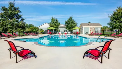 Circular swimming pool with red loungers and green umbrellas at Reserve at Mill Creek's outdoor lounge area