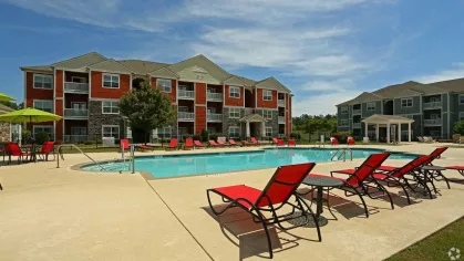 Sunny poolside view with red chairs and umbrellas next to red-and-beige apartment buildings