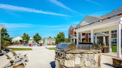 Stone grill station under a white pergola beside the pool and red apartment buildings