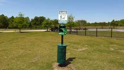  Open grassy dog park with pet waste station and black metal fencing under a clear blue sky.