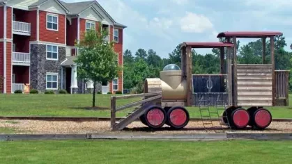  Outdoor playground with red train-shaped play structure in front of red apartment buildings
