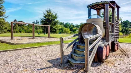 Wooden train and swing set in shaded community playground with mulch ground covering.
