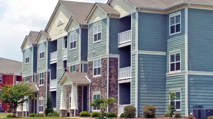 Side view of green apartment buildings with stone base accents and landscaped green space.