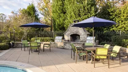 Poolside grilling station and dining area at The Heights at Lake Murray featuring stone fireplace, stainless steel grills, and umbrella-covered seating