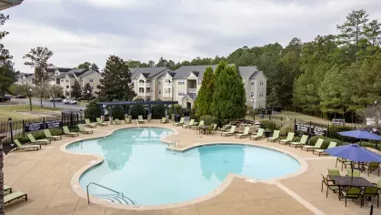 Aerial view of community pool at The Heights at Lake Murray with surrounding apartments and forested backdrop