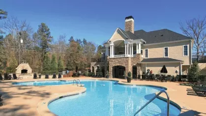 Sunny day view of sparkling pool at The Heights at Lake Murray with classic-style clubhouse and shaded lounge seating