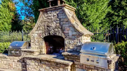 Outdoor stone fireplace and stainless steel grill setup at The Heights at Lake Murray’s poolside grilling area