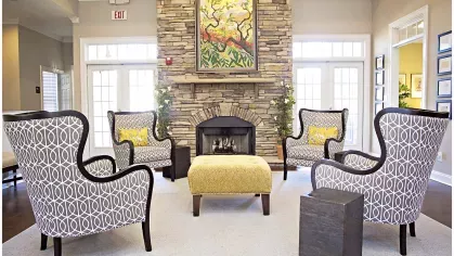 Warm and inviting clubhouse fireplace lounge at The Heights at Lake Murray with four patterned armchairs and central ottoman
