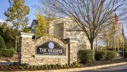 Welcome sign for The Heights at Lake Murray luxury apartment rentals framed by stone pillars, seasonal flowers, and American flags