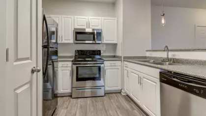 Modern kitchen with stainless steel appliances, granite countertops, and white cabinetry at The Saulet Apartments in New Orleans, LA.