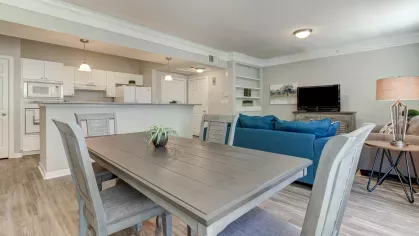 Open-concept dining and living area with view into a modern kitchen at The Saulet Apartments in New Orleans.