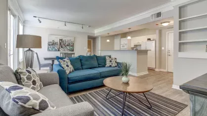 Stylish living room setup with crown molding, open layout, and direct access to the kitchen at The Saulet Apartments.