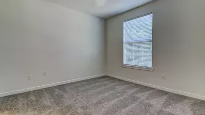 Spacious empty bedroom with large window and soft carpeting at The Saulet Apartments, ready for your personal touch.