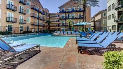 Outdoor pool area with plenty of seating and palm trees, surrounded by colorful apartment buildings at The Saulet Apartments.