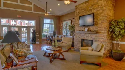 Cozy clubhouse interior at Knob Creek Apartments featuring a stone fireplace, plush seating, and large windows for natural light.
