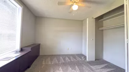  Empty bedroom with neutral carpet, built-in closet and shelving, ceiling fan, and a large window at Astorwood Apartments.