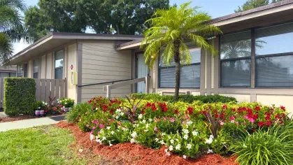 Side view of Astorwood Apartments leasing office surrounded by tropical landscaping, flowering plants, and neatly trimmed grass.