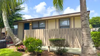 Apartment home at Astorwood Apartments with a fenced-in patio entrance, tropical trees, and manicured lawn under a bright blue sky.