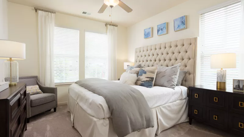 Primary bedroom at Avery Turkey Creek Apartments with tufted headboard, plush bedding, and large windows.