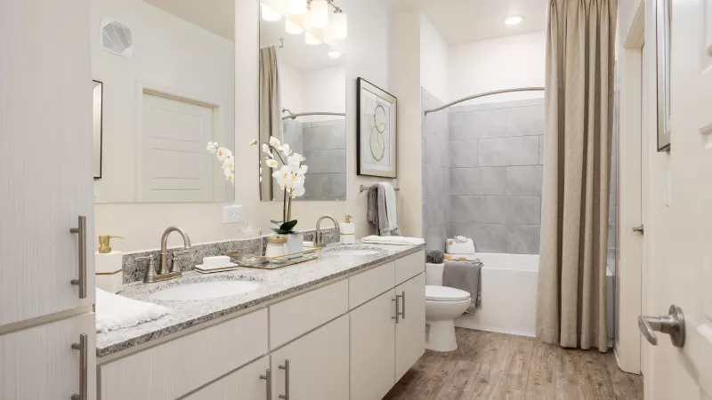 Luxury bathroom at Avery Turkey Creek Apartments with double vanity sinks, granite countertops, and tiled shower-tub combination.