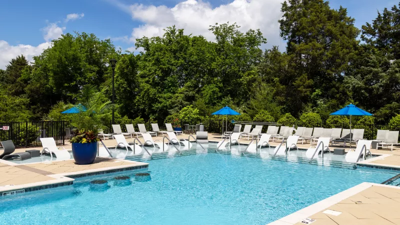 Outdoor pool at Avery Turkey Creek with in-water lounge chairs and surrounding deck chairs under blue umbrellas.