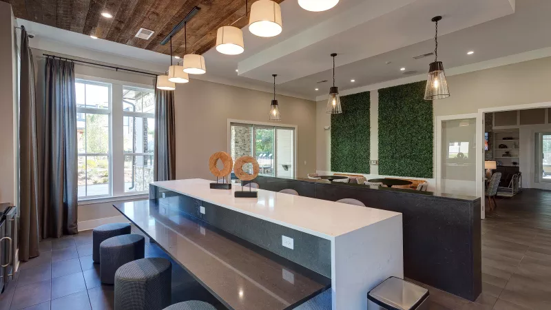 Clubhouse social area with bar seating, pendant lighting, and greenery accent wall at Avery Turkey Creek.