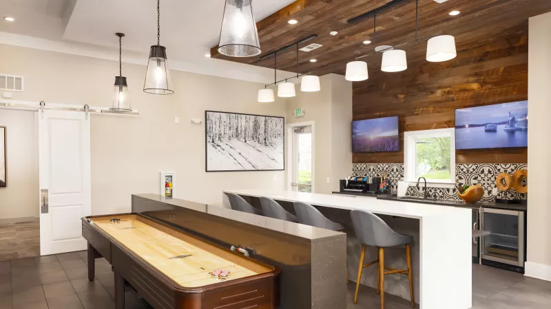 Resident game lounge at Avery Turkey Creek with shuffleboard table, bar seating, and pendant lighting.